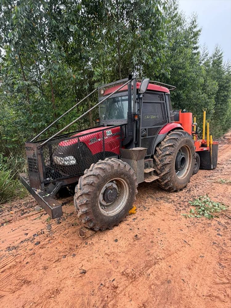 Trator florestal com grade de proteção estacionado em estrada de terra entre talhões de eucalipto